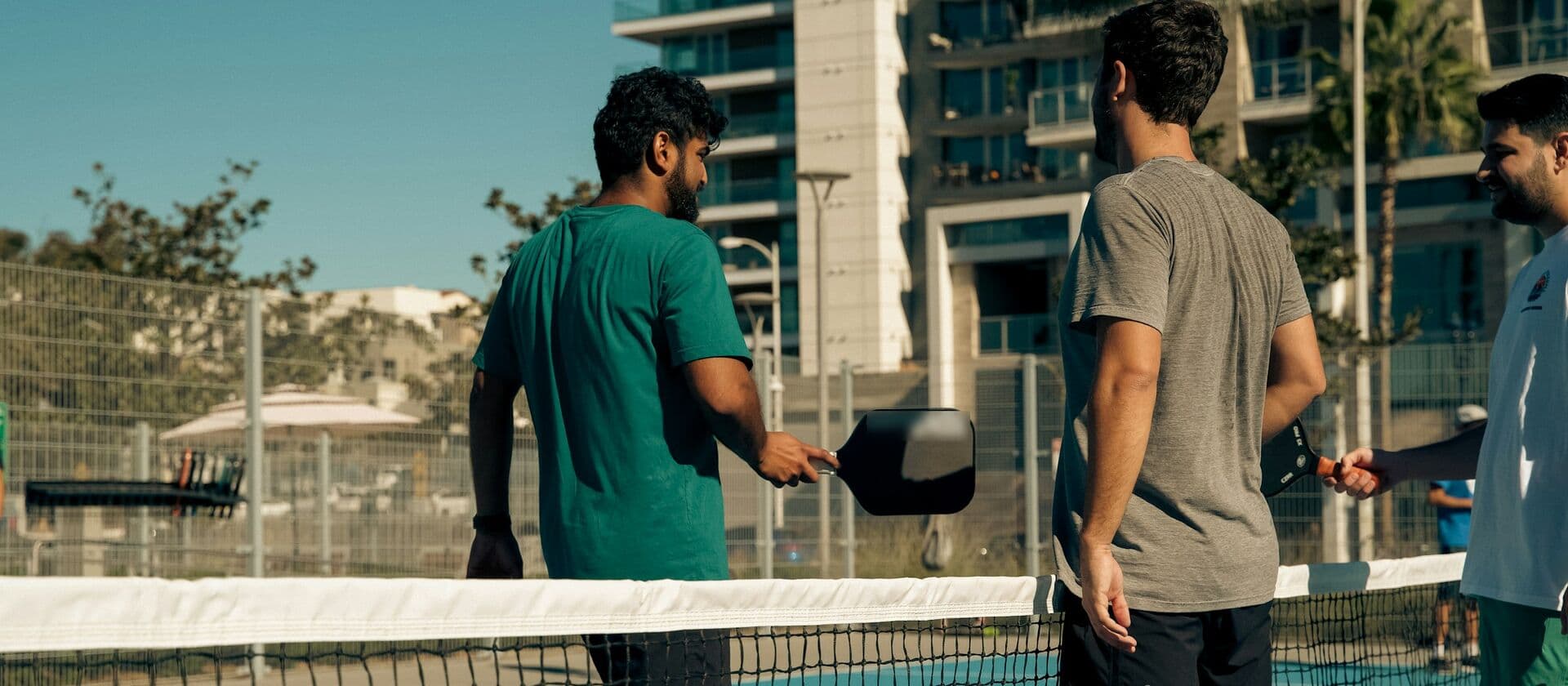 Tres jugadores de pickleball chocan las palas sobre la red al terminar un partido